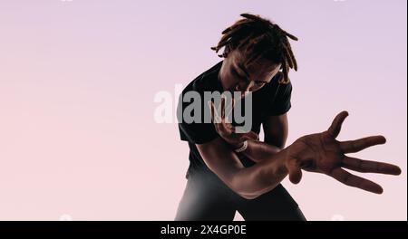 Der rhythmische Gen Z Männchen tanzt energetisch in einem Studio, seine expressiven Bewegungen erzeugen eine künstlerische Silhouette vor rosa Hintergrund. Stockfoto