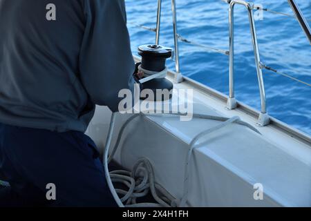 Der Mann zieht ein Seil an der Seilwinde des Segelbootes, Yachtdetails. Yachting Stockfoto