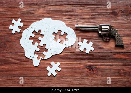 Revolver liegt neben einem menschlichen Gehirn-förmigen Puzzle vor einer strukturierten Holzkulisse. Mehrere fehlende Puzzleteile liegen auf dem Tisch, was das noch verstärkt Stockfoto