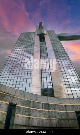 Die Pracht eines Art déco-Wolkenkratzers wird vor der Leinwand eines dramatischen Sonnenuntergangs verwundert. Das reflektierende Glas des Gebäudes fängt das verblassende Licht ein, während architektonische Details sich in den leuchtenden Farben der Dämmerung abheben. Dieses Bild feiert die Kreuzung von historischem Design und Naturschauspiel. Art déco-Wolkenkratzer erhebt sich vor einem dramatischen Sonnenuntergangshimmel. Hochwertige Fotos Stockfoto