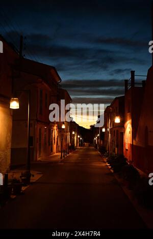 Eine ruhige abendliche Straßenszene, beleuchtet von Straßenlaternen, die die ruhige Atmosphäre eines malerischen Dorfes in der Abenddämmerung einfangen Stockfoto