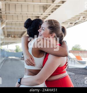 Zwei Frauen in Übergröße in Sportbekleidung, die sich nach einem Workout umarmen. Lächelnde Frau in roter Sportswear, die sich beim Training mit ihrem Freund umschließt Stockfoto