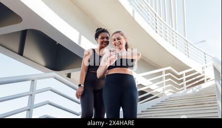 Glückliche Frau in Übergröße, die ihre Freundin beim Workout auf Smartwatches zeigt. Zwei Freunde in Sportbekleidung sehen sich Smartwatches an. Glückliche Frau in Übergröße Stockfoto