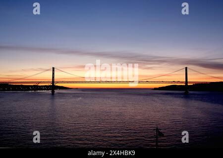 40 Uhr Sonnenaufgang über der Brücke zum 25. Jahrestag, Fluss Tejo, Lissabon, von einem sich nähernden Kreuzfahrtschiff aus gesehen, April 2024. Stockfoto