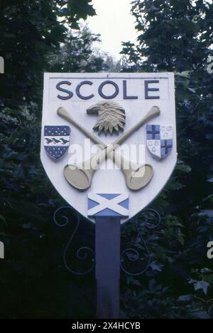 Norfolk/Suffolk. 1987: Ein Foto des Dorfzeichens Scole an der Grenze zwischen Norfolk und Suffolk. Das Schild ist mit gekreuzten Pfostenhörnern verziert, die das Scole Inn, das älteste Gebäude der Gemeinde, darstellen. Scole liegt 30 km südlich von Norwich am Nordufer des Flusses Waveney. Es liegt an der alten Römerstraße nach Venta Icenorum. Stockfoto