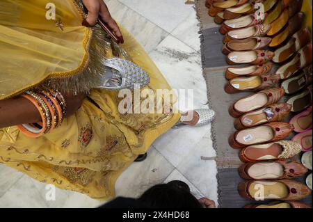 Wunderschöne indische Rajasthani-Frau, die ihren Fuß ausprobiert, um farbenfrohe Rajsathani-Damenschuhe im Schuhgeschäft auf dem berühmten Sardar-Markt anzubringen. Stockfoto