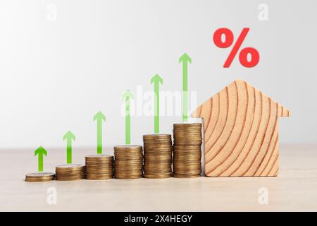 Hypothekenzinssatz. Hölzernes Modell des Hauses, gestapelte Münzen, Pfeile und Prozentzeichen Stockfoto
