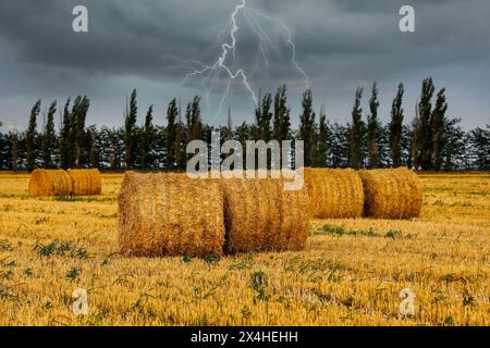 Heuballen auf dem Feld unter stürmischem Himmel mit Lichtern Stockfoto