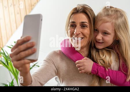 Lächelnde Mutter und Tochter umarmen und ein Selfi mit dem Smartphone machen Genießen Sie einen lustigen Moment Stockfoto
