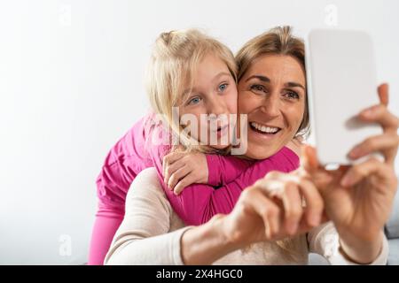 Mutter und Tochter genießen eine enge Umarmung, während sie ein Selfie machen, beide lächeln fröhlich Stockfoto