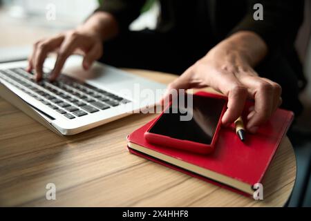 Eine männliche Hand tippt auf dem Laptop, während eine andere das Telefon auswählt Stockfoto