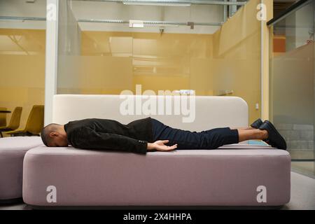 Müder männlicher Angestellter, der im Büro auf dem Sofa schläft Stockfoto