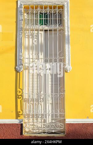 227 die Sonne am späten Nachmittag beleuchtet den weißen Grill und die geschlossene Holzblende eines Fensters, die gelbe Wand eines Kolonialhauses. Trinidad-Kuba. Stockfoto