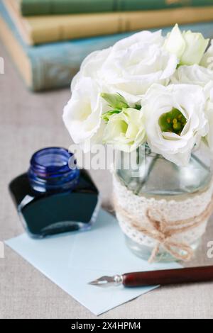 Strauß aus weißen Eustoma-Blüten, Flasche Tinte und Vintage-Stift. Stapel Bücher im Hintergrund. Stockfoto