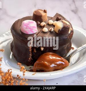 Argentinisches Alfajor bedeckt mit Schokolade mit Bonbons und einem Löffel Dulce de leche auf einem weißen Teller Stockfoto