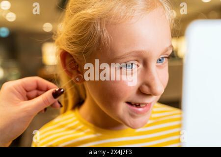 Ein Mädchen lächelt, während er einen Ohrring anprobiert, mit Hilfe eines Mitarbeiters in einem Juweliergeschäft Stockfoto