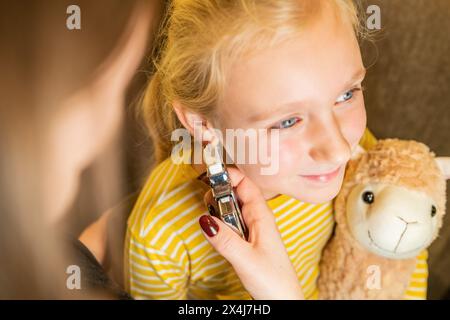 Kind hält einen Teddybären, während er sich in einem Juweliergeschäft von einem professionellen medizinischen Mitarbeiter das Ohr durchbohrt Stockfoto