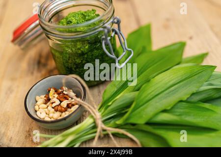 Glas mit wildem Knoblauchpesto mit Pinienkernen, Walnüssen und frischen Blättern auf einem Holztisch Stockfoto