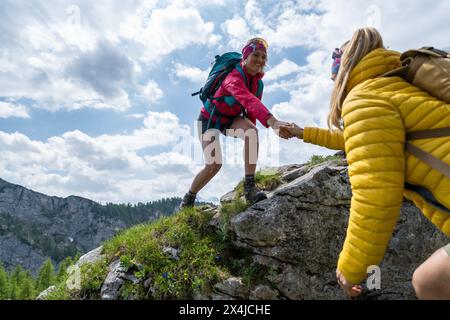 Helfende Handwandererin, die Hilfe beim Klettern auf einem felsigen Hang in den Bergen bekommt. Wandern und Teamwork-Konzept. Stockfoto