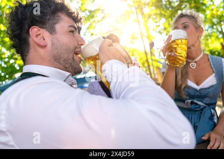 Mann und Frau in traditioneller bayerischer Kleidung trinken Bier im Biergarten oder oktoberfest Stockfoto