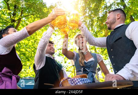 Gruppe glücklicher bayerischer Freunde, die Bier im Biergarten in deutschland trinken und toasten Stockfoto