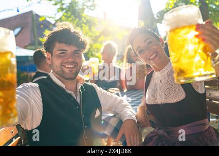 Mann und Frau in traditioneller deutscher Kleidung mit Bierbecher, mit Sonnenlicht auf dem oktoberfest oder Biergarten in bayern Stockfoto
