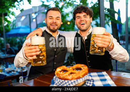 Im Biergarten oder Oktoberfest - glückliche Freunde in Tracht, Dirndl und Lederhosen trinken frisches Bier in Bechern in Bayern Stockfoto