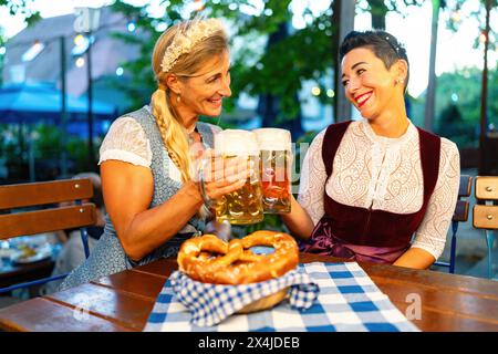 Bayerische Freundinnen in Tracht oder Dirndl, das bei Bier im Biergarten oder oktoberfest in Bayern tobt Stockfoto