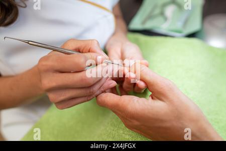 Nahaufnahme eines Manikürs mit einem Nagelhautschieber auf dem Fingernagel eines Kunden Stockfoto