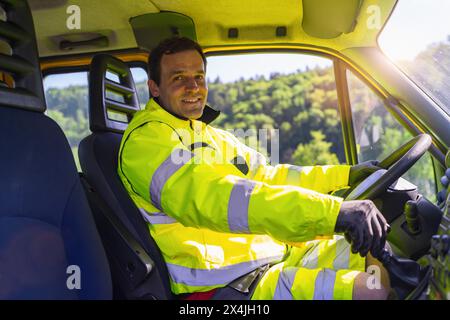 Lächelnder Fahrer des Abschleppwagens in reflektierender Sicherheitsausrüstung in der Fahrerkabine Stockfoto