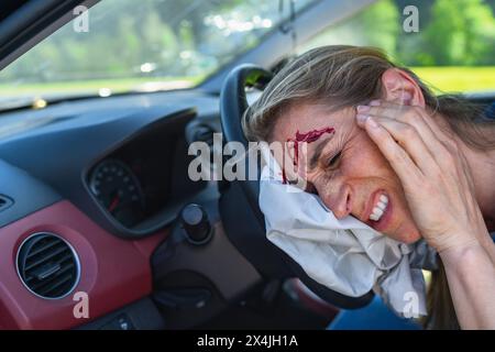 Verletzte Frau mit Kopfwunde, die in einem abgestürzten Auto sitzt Stockfoto