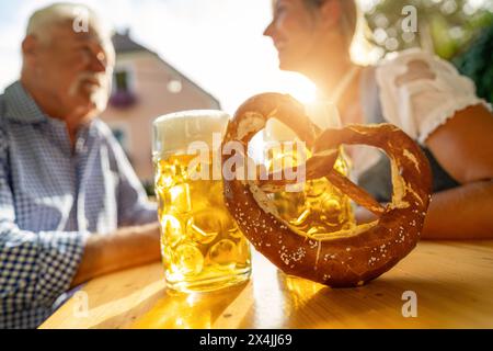 Bayerische Bierbecher und Brezel auf dem Tisch mit älteren Männern und Frauen im Hintergrund im Biergarten in München Stockfoto