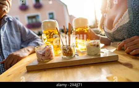 Traditionelle bayerische Obatzda mit Brezeln und Radieschen und Bierbecher, Seniorenmann und Frau im Hintergrund im Biergarten oder oktoberfest, München, G Stockfoto