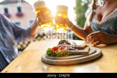 Bayerische Obatzda mit Brezeln und Radieschen und Bierbecher, Mann und junge Frau in tracht im Hintergrund beim Biergarten oder oktoberfest, München, Keim Stockfoto