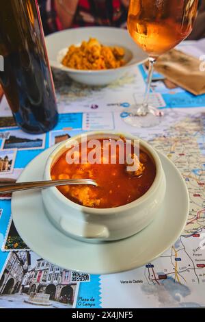 Ein Teller mit appetitlicher Suppe in einer Reiseumgebung, mit einem Tischset, das verschiedene Touristenziele zeigt, wodurch eine interessante Mischung aus Speisen und To entsteht Stockfoto