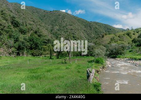 Landschaft eines grünen Tals, umgeben von Bergen mit einem Fluss, der durchfließt, und einem blauen Himmel Stockfoto