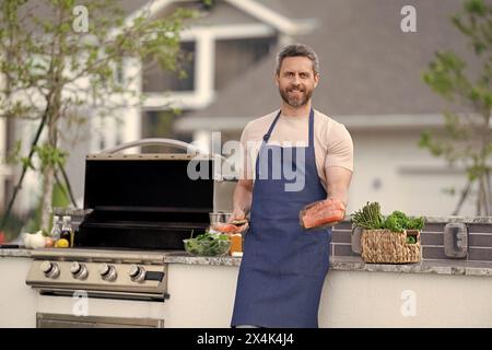 Koch mit gegrilltem Lachs, Kopierraum. Küchenchef, der gegrillten Lachs im Freien kocht. Gegrillter Lachsfisch bei man Wear Chef Schürze. Foto vom Koch mit gegrilltem Essen Stockfoto