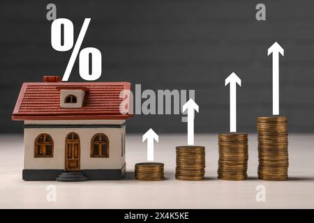 Hypothekenzinssatz. Modell des Hauses, gestapelte Münzen, Pfeile und Prozentzeichen Stockfoto