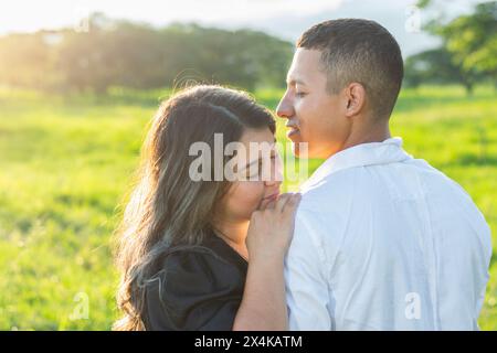 Ein junges lateinisches Paar, eine Frau, die sich auf die Schulter ihres Mannes stützt, während sie die Augen schließt, Sonnenuntergang im Hintergrund Stockfoto