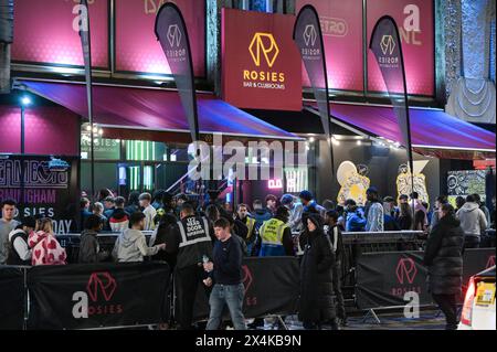 Broad Street, Birmingham, 4. Mai 2024 - am Freitagabend besuchten die Revellers den berüchtigten Nachtclub von Birmingham, um die Feiertage Anfang Mai zu beginnen. Der Regen hat die Partygäste nicht davon abgehalten, sich mit Mänteln oder Handtaschen zu amüsieren, um ihre Haare vor den Elementen zu schützen. Zwei Jungs saßen an einer Bushaltestelle mit einem Pappausschnitt von Louis Tomlinson, den sie aus einem Nachtclub in der Nähe hatten. Der Nachtclub Rosies war besonders voll mit Warteschlangen, die sich um Barrieren schlängelten. Zwei spärlich bekleidete Feuerschauer unterhielten Passanten im Walkabout und die Pubbesucher genossen Musik in Heidi's Bier Bar, während sie tanzten Stockfoto