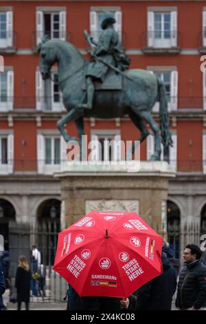 Madrid, Spanien. Februar 2024 - Reiseleiter mit rotem Regenschirm vor der Reiterstatue am Plaza Mayor Stockfoto