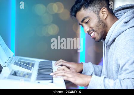 Indischer Mann, Musik und glücklich mit Tastatur oder Instrument für Geschicklichkeitsübungen, Talent und Leidenschaft. Musiker, Probe und Lächeln oder zufrieden mit Karriere Stockfoto