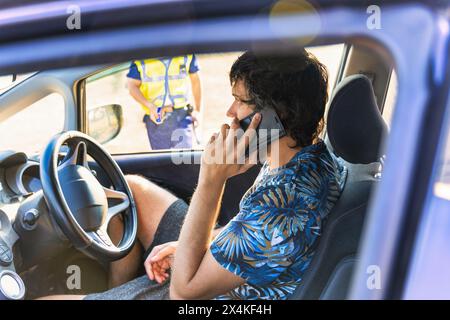 Weißer Mann im Auto, der auf der Straße telefoniert, Polizist vor Ort, wartet auf Hilfe von der Versicherung, in südafrika Stockfoto