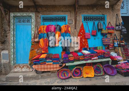 Marokkanisches handgefertigtes Kunsthandwerk, Teppiche, Kleidung, Taschen und andere Produkte hängen über der Wand auf den Straßen von Chefchaouen Medina in Marokko Stockfoto