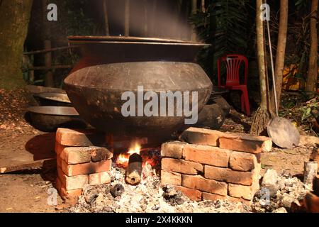 Kochen über Nacht in einer Dorfparty auf einem temporären Backofen. Im Freien kochen für viele Menschen in einer großen Aluminiumpfanne im Holzfeuer. Riesiger Kochtopf Stockfoto