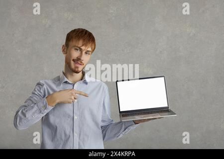 Porträt eines positiven jungen Mannes, der Laptop mit leerem weißen Bildschirm hält und in die Kamera lächelt. Stockfoto