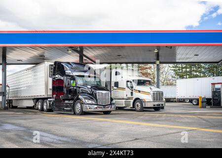 Industrietransporter verschiedene große Lkw-Sattelzugmaschinen mit beladenen Aufliegern stehen in Reihe auf der Tankstelle des Lkws und füllen Tanks bis Stockfoto