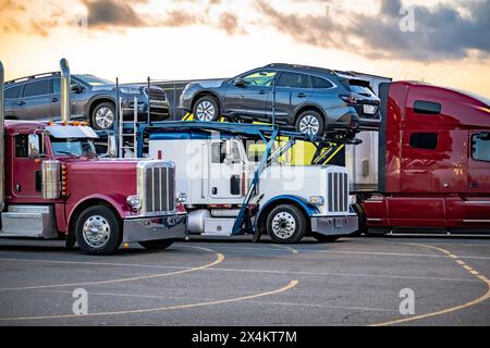 Industrietransporter verschiedene große Lkw Sattelzugmaschinen mit beladenen Aufliegern stehen in Reihe auf dem LKW, halten Parkplatz zur Abendzeit tak Stockfoto