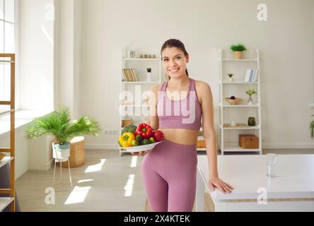 Schöne sportliche Frau, die sich an gesunde Ernährung hält, hält Teller mit frischem Gemüse. Stockfoto