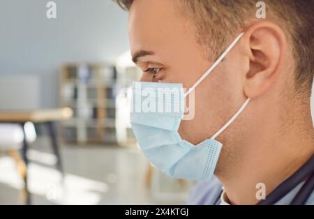 Nahaufnahme Porträt des nachdenklichen Mannes Arzt oder Krankenschwester in blauer Gesichtsmaske, die im Büro steht. Stockfoto
